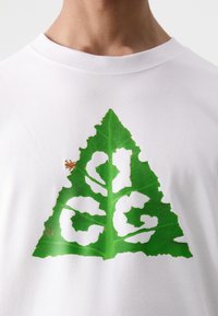 White short-sleeve t-shirt featuring a large green leaf graphic with white accents. Notable small brown detail in the design.