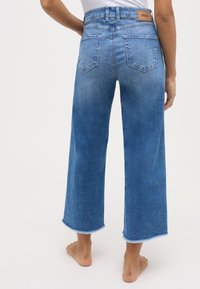 Wijde, lichtblauwe denim jeans met een rafelige zoom; vijf zakken en een gevoerd bruin leren label op de achterste tailleband.