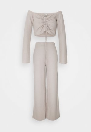 Beige geribd gebreid tweedelig set met een off-shoulder crop top met lange mouwen en plooitjes aan de voorkant, en bijpassende hoge taille broek met wijde pijpen.