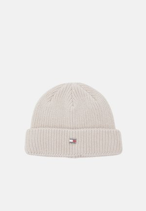Gorro tipo beanie en punto beige claro. Presenta una textura acanalada y un puño plegado. Etiqueta de logo pequeña en la parte frontal.