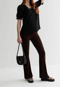 Blouse noire à boutons avec des manches bouffantes, associée à un pantalon évasé marron chocolat. Accessoirisée avec un sac à main matelassé noir et des sandales chunky.
