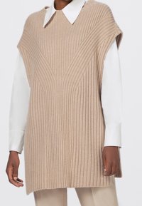 Beige gestrickte Sweaterweste mit einer gerippten Textur, V-förmigen Designdetails und kurzen Ärmeln, über einem weißen Hemd mit Kragen getragen.