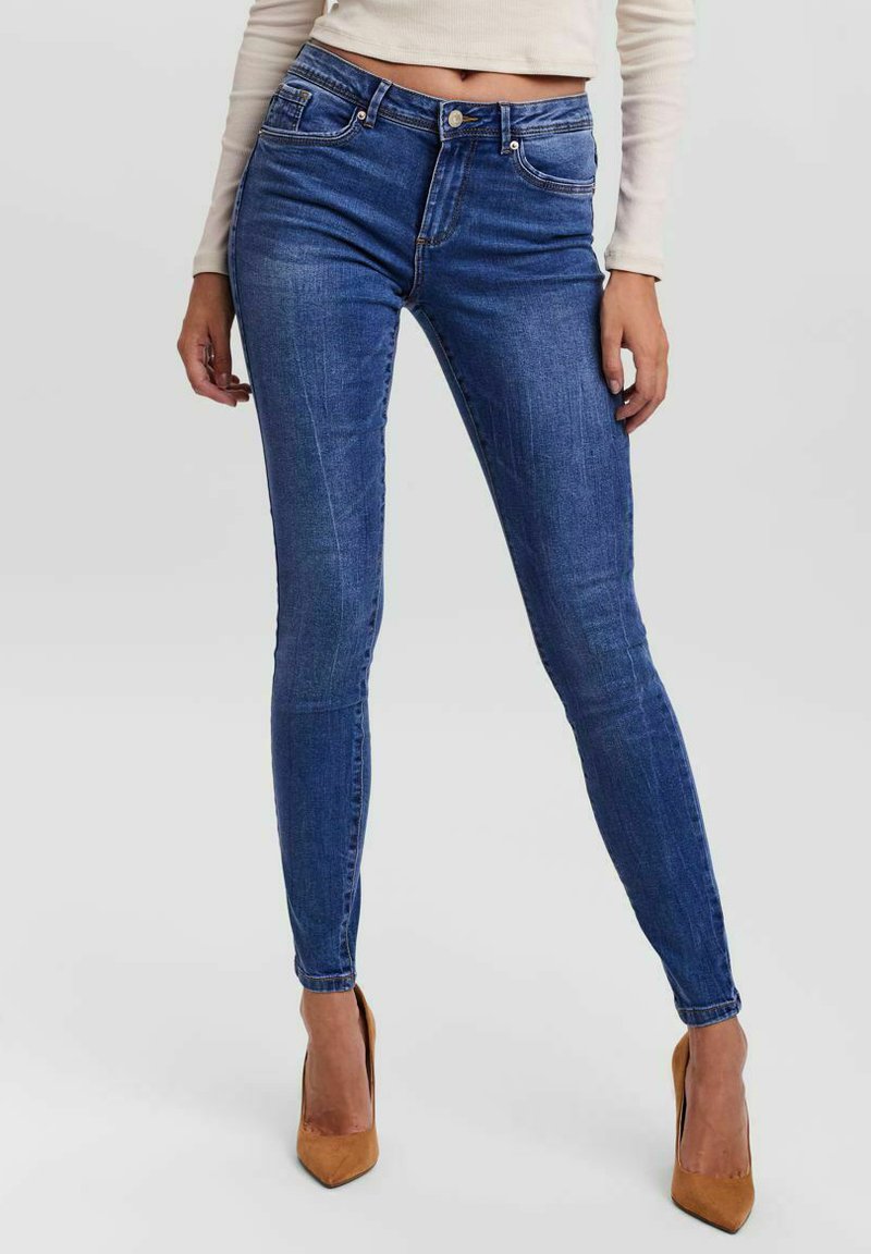 Jeans de mezclilla azules ajustados con diseño de cinco bolsillos, ligeros desgastes y detalles de costura. Combinados con tacones color beige de punta afilada.