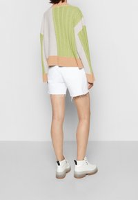 Gebreide trui in groen, beige en grijze strepen met een chunky textuur. Gecombineerd met witte spijkerhortens en witte enkelboots met zwarte accenten.