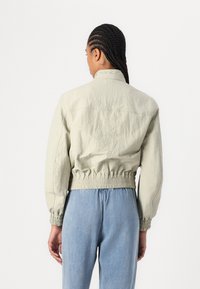 Veste cropped gris clair avec taille élastique et poignets, dotée d'un col simple et d'une texture lisse. Assortie avec un pantalon en denim bleu.
