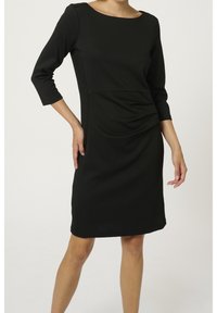 Robe noire avec des manches trois-quarts, tissu avant lisse, détails froncés sur les côtés et accents côtelés texturés le long des côtés.