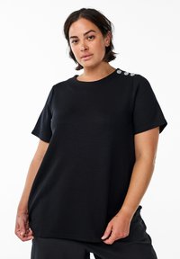 Black short-sleeve t-shirt with a relaxed fit, featuring decorative hardware accents on the shoulder, made from soft, textured fabric.
