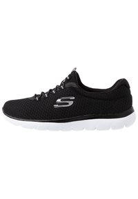 Chaussure de sport noire avec une tige en maille, design à lacets, semelle blanche et logo argenté sur le côté. Conçue pour le confort et la flexibilité.
