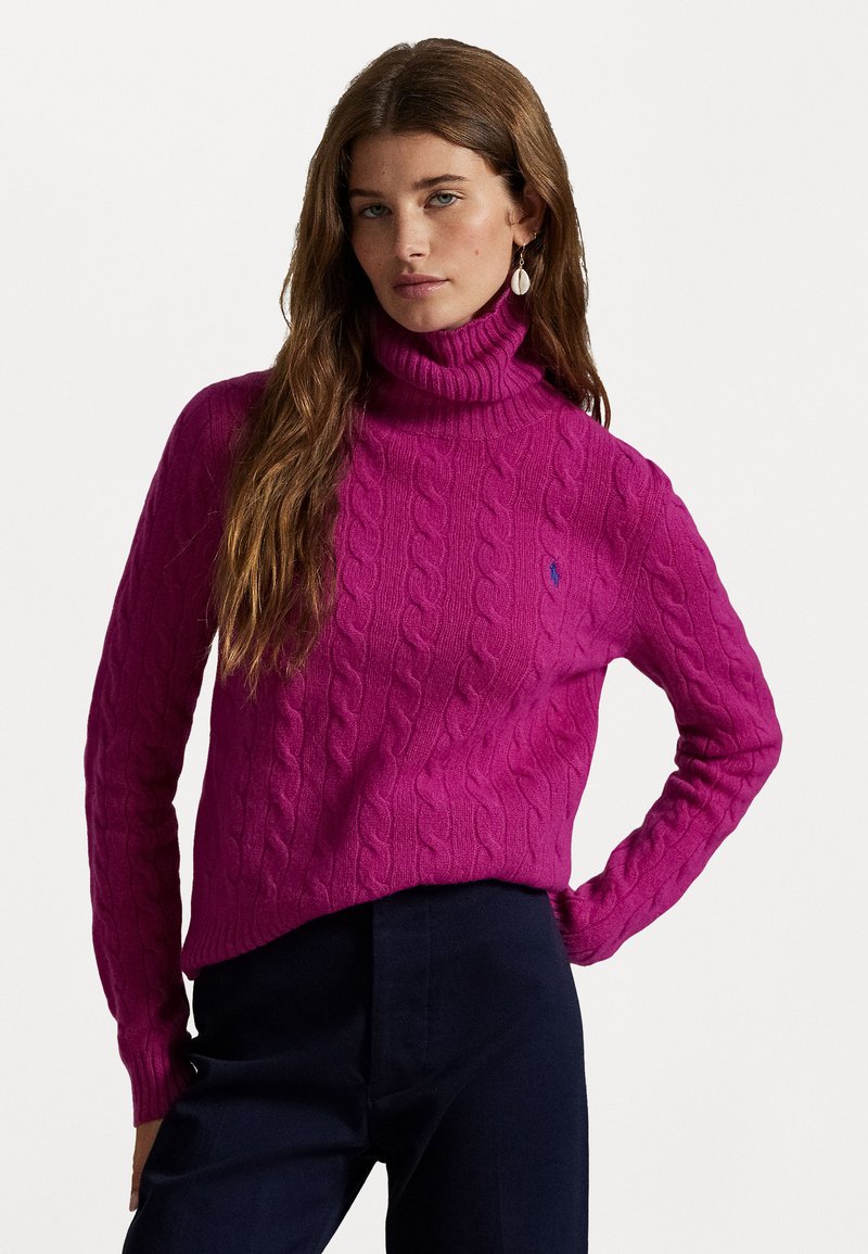 Pulover tricotat fucsia cu guler înalt, prezentând un model cu puncte de cablu. Textură moale cu o croială lejeră, asortat cu pantaloni închisi.
