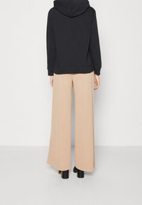 Felpa nera con cappuccio e tasca a marsupio, abbinata a pantaloni beige a gamba larga. Il tessuto sembra morbido, presenta una vestibilità rilassata e maniche lunghe.