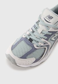 Light blue mesh running shoe with grey accents, textured suede details, and a cushioned sole. Features laces and a logo on the tongue.