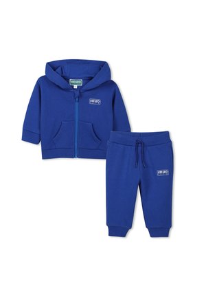 Blauwe katoenen trainingsoutfit met een rits-hoodie met voorzakken en bijpassende broeken met een elastische tailleband. Beide hebben logo-accenten.