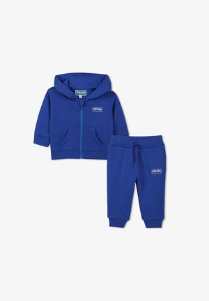 Ensemble de survêtement en coton bleu comprenant un hoodie zippé avec poches avant et un pantalon assorti avec une taille élastique. Les deux pièces comportent des accents de logo.