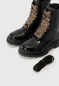 Sorte patentlær ankleboots med leopardmønstrede snørebånd og glidelås på siden. Inkluderer ekstra svarte skolisser. Kraftig såle for stabilitet.