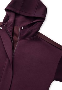 Bordeauxroter Kapuzenpullover mit Reißverschluss vorne, mit glatter Textur, kontrastierenden Schulterpaneelen und Druckknopfdetails.