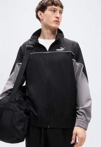 Μαύρο και γκρι αθλητικό μπουφάν με φερμουάρ, ψηλό γιακά και ελαστικά μανίκια. Διαθέτει λευκή επένδυση και το λογότυπο Puma στο στήθος.