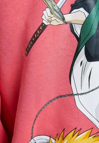 Grafisk t-shirt med en detaljerad illustration i livliga färger. T-shirten har en rosa bakgrund, med en karaktär som håller ett svärd.