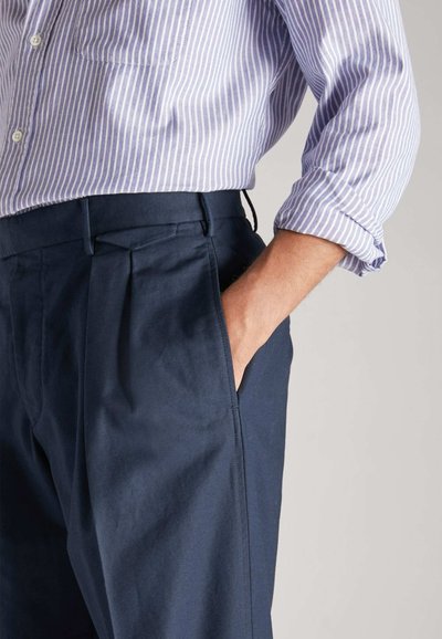 Pantalones navy con una textura suave, que presentan pliegues frontales y bolsillos laterales, combinados con una camisa de botones a rayas morada clara.