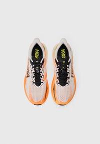 Chaussures de sport avec une tige en mesh respirant de couleur blanche, orange et noire, dotées d'un système de laçage et d'une semelle rembourrée pour le confort.