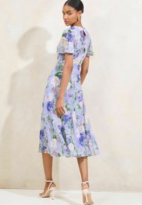 Lila bloemen midi-jurk met korte mouwen, een sleutelgat aan de achterkant en een zwierige zoom. Bevat blauwe en roze rozen overal. Gecombineerd met nude hakken.