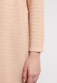 Ljus persikofärgad stickad topp med en strukturerad ribbad design och trekvartslånga ärmar, som framhäver det mjuka tyget och en bekväm passform.