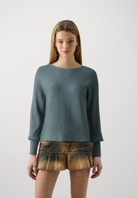 Pull en bleu doux avec texture côtelée, col rond et manches longues. Associé à une jupe en denim courte et plissée avec un design décoloré.
