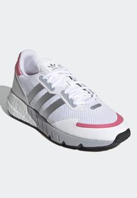 Vit sportskor med överdel i mesh, rosa och grå detaljer, tre grå ränder och en dämpad sula. Har en snörningsdesign.