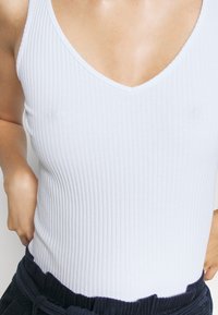 Vit ribbad linne med V-ringning, figurnära form och mjuk textur, kombinerad med marinblått tyg i midjan.