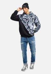 Black hoodie with a textured gray design, blue jeans with distressing, and black and white patterned high-top sneakers.