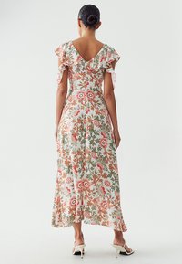 Robe maxi fleuri en tissu léger, avec des manches volantes et un dos en V. Les couleurs incluent du rose, de l'orange et du vert sur un fond clair.
