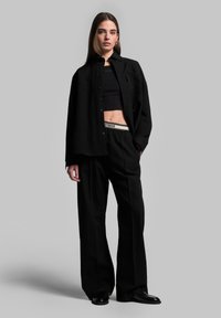 Zwarte overhemd met knopen over een zwart cropped top, gecombineerd met brede zwarte broek met een witte merkband; gladde stoftextuur.