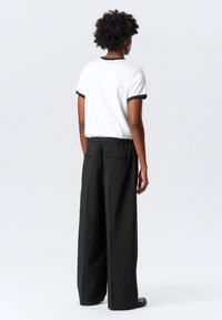 Pantalones anchos negros con cintura elástica, combinados con una camiseta ajustada blanca que presenta acentos ribeteados negros en las mangas y el cuello.