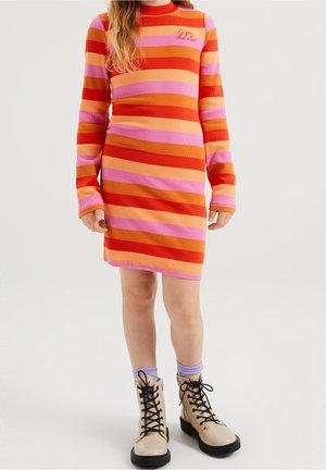 Robe côtelée rayée aux couleurs orange, rose et rouge, avec des manches longues et un texte brodé. Associée à des bottines beiges à lacets.