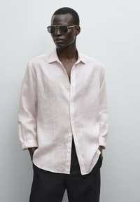Light pink linen button-up shirt with a relaxed fit and long sleeves, paired with black pants and sunglasses. Minimalistic design.