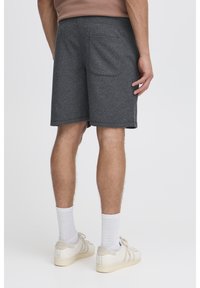 Pantaloncini grigi in misto cotone con elastico in vita, tasca posteriore e vestibilità comoda, abbinati a calzini bianchi e sneakers chiare.