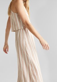 Olkaimeton, lyhyt paita, jossa pystysuorat raidat beigen ja ruosteen sävyissä. Hento ja väljä maksihame, valmistettu kevyestä kankaasta.