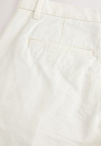 Pantaloni bianchi in cotone con una tasca posteriore visibile e una cucitura pulita. Il tessuto è liscio con una leggera trama.