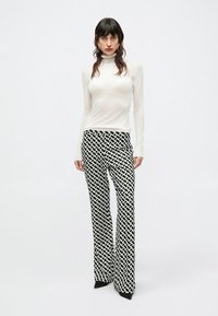 Balta garām piedurknēm ar augstu apkakli, kas kombinēta ar melnām un baltām rakstainām paplašinātām biksēm. Biksēm ir savienotas ovālas formas un gluda auduma tekstūra.