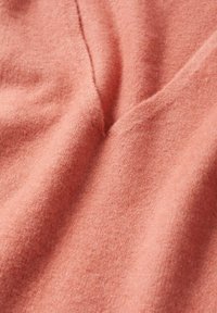 Miękka, koralowa tkanina o gładkiej fakturze, z delikatnym połyskiem i łagodnym układem. Brak widocznych wzorów czy elementów metalowych.