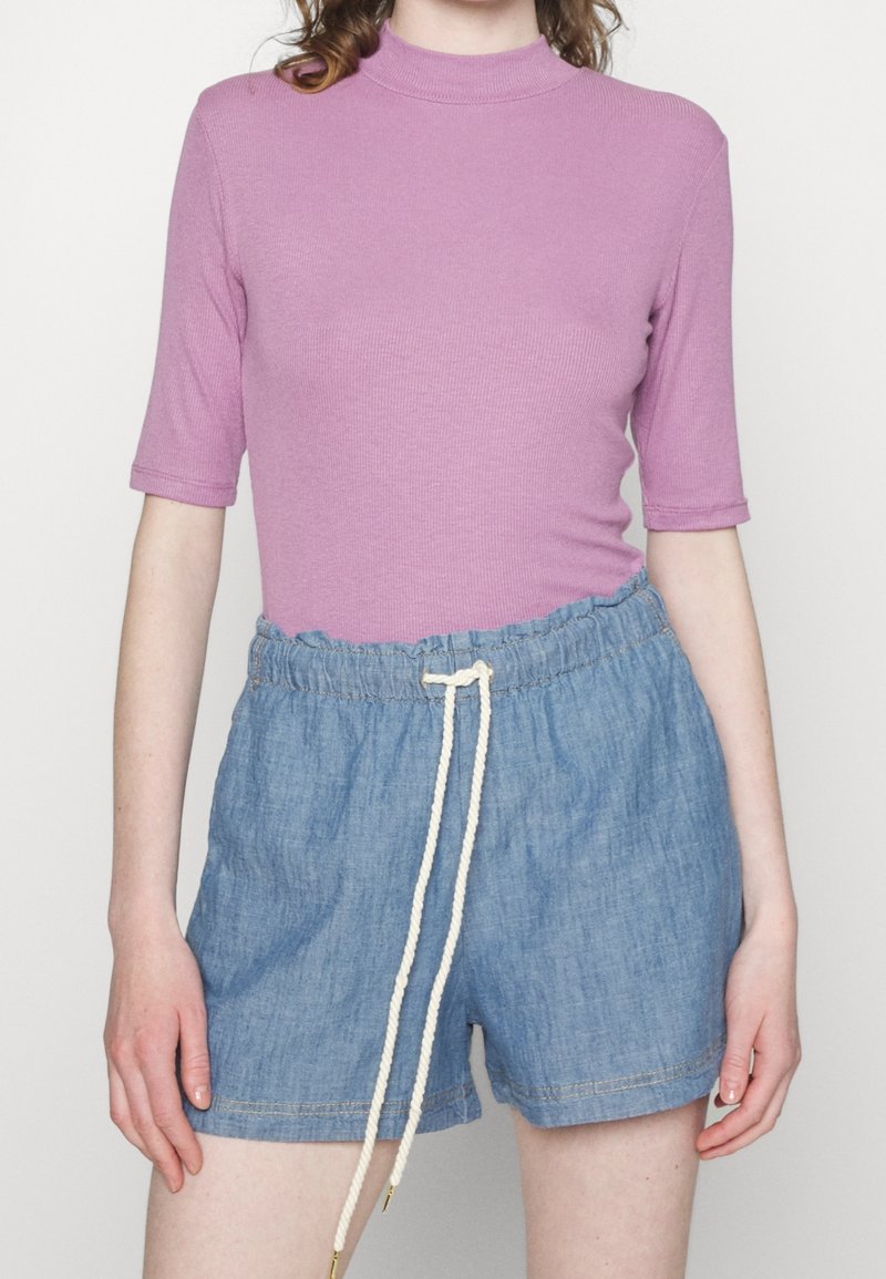 Femme portant un haut rose ajusté à manches courtes et un short bleu à taille élastique avec un cordon blanc.