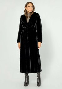 Černý umělý kožich s dlouh�ými rukávy, velkým límcem a přímým střihem, kombinovaný s černými kozačkami na podpatku do výšky kolen.