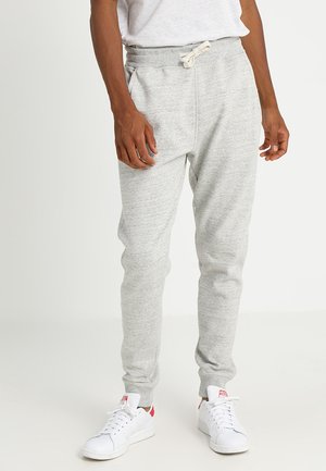 Gray sweatpants made of soft fabric, featuring an elastic waistband with drawstring, tapered legs, and ribbed cuffs. Worn with white sneakers.