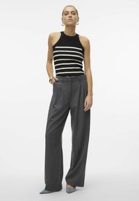 Černobíle pruhovaný žebrovaný crop top doplněný o šedé široké kalhoty s vysokým pasem a světle modré lodičky s špičatou špičkou.