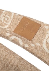 Bufanda de color beige con un patrón que presenta una tela texturizada y una etiqueta de cuero con el lema "LIU JO desde 1995" estampado.