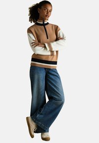 Beež, vetrupp-hõlmaga sviiter, millel on valged varrukad ja tumesinine lisatud. Kombineeritud laia jalgadega siniste teksade ja beežide tossudega. Sujuv tekstuur, mugav istuvus.