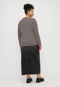 Camiseta de largas mangas a rayas marrones y blancas, combinada con una falda maxi de mezclilla negra. Detalles destacados incluyen un sencillo cuello redondo y costura lateral.