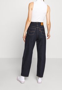 Mörkblå högmidjadejeans med rak benlängd, med bakfickor och kontrasterande sömmar, kombinerade med vita sneakers och en ärmlös topp.