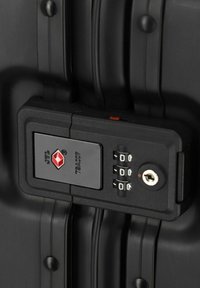Schwarzes TSA-zugelassenes Schloss mit einem Ziffernfeld für die Eingabe von Zahlen, ausgestattet mit einem Schlüsselloch und einem geprägten Logo. Montiert auf einer strukturierten schwarzen Kofferoberfläche.
