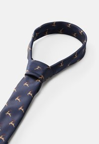 Ναυτικό μεταξωτό λαιμόκομπο με επαναλαμβανόμενα σχέδια ταρανδώων σε χρώμα καφέ. Η υφή είναι λεία με γυαλιστερό φινίρισμα. Κλασικός σχεδιασμός με κλειστού τύπου κόμπο.