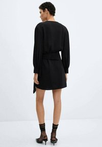 Black dress with long sleeves, tie waist detail, and above-knee length. Soft fabric with a smooth texture, featuring buttoned cuffs.